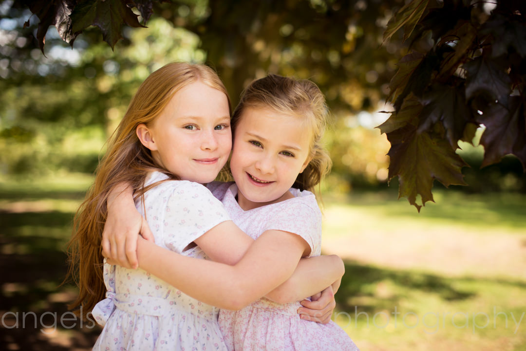 family photographer in welwyn garden city captures sisters cuddling in countryside setting