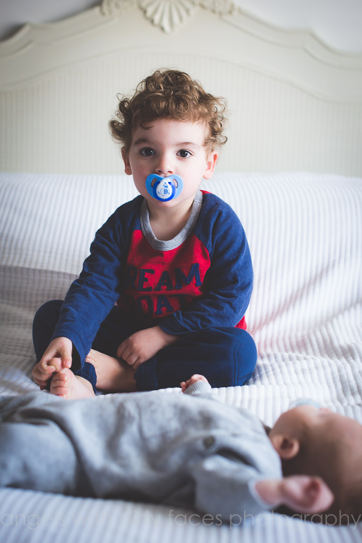 two brothers sit on the bed with their dummies in their mouths