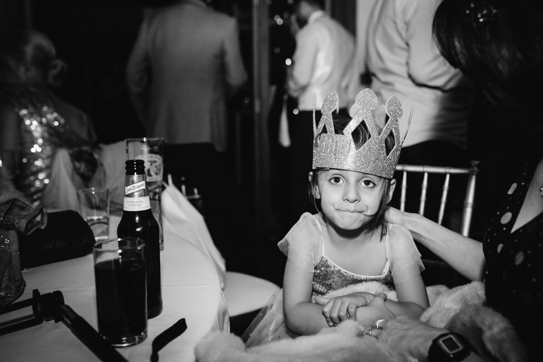 Child at a wedding reception wearing a bored expression and party hat