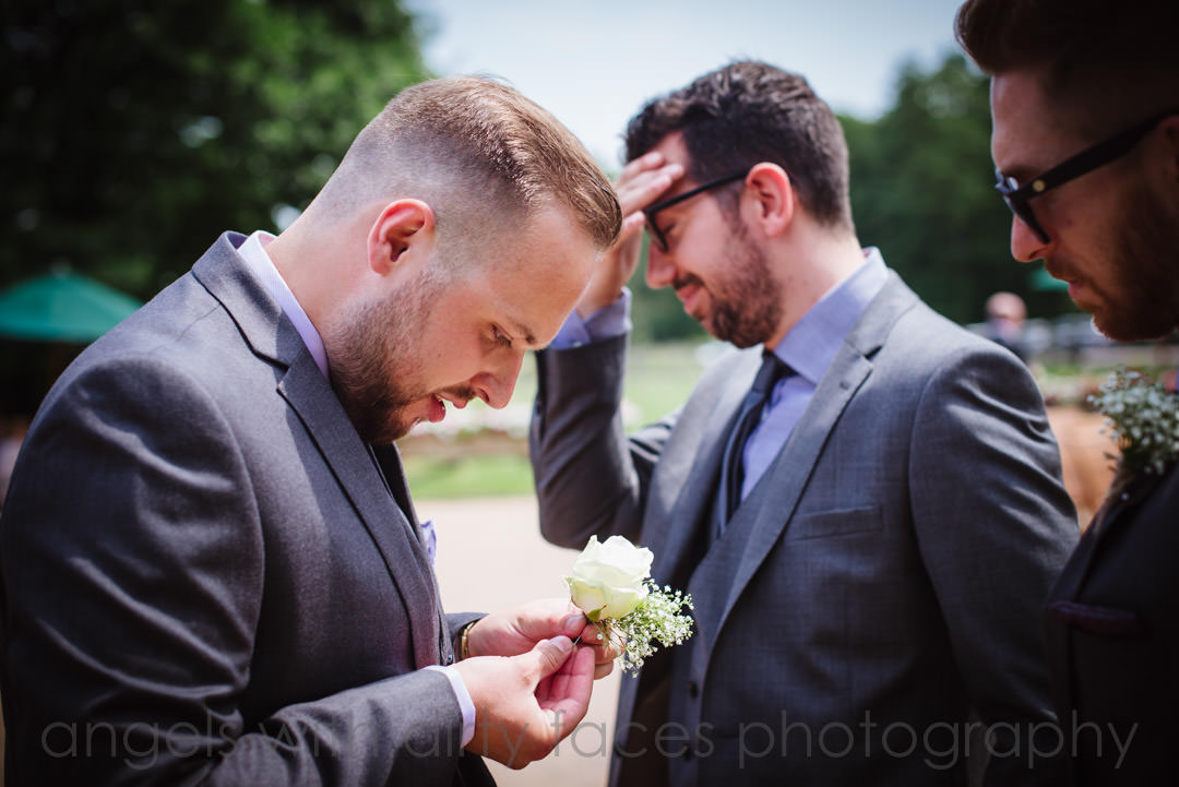 tewin bury farm  hotel wedding photography showing groomsmen trying to put on a button hole