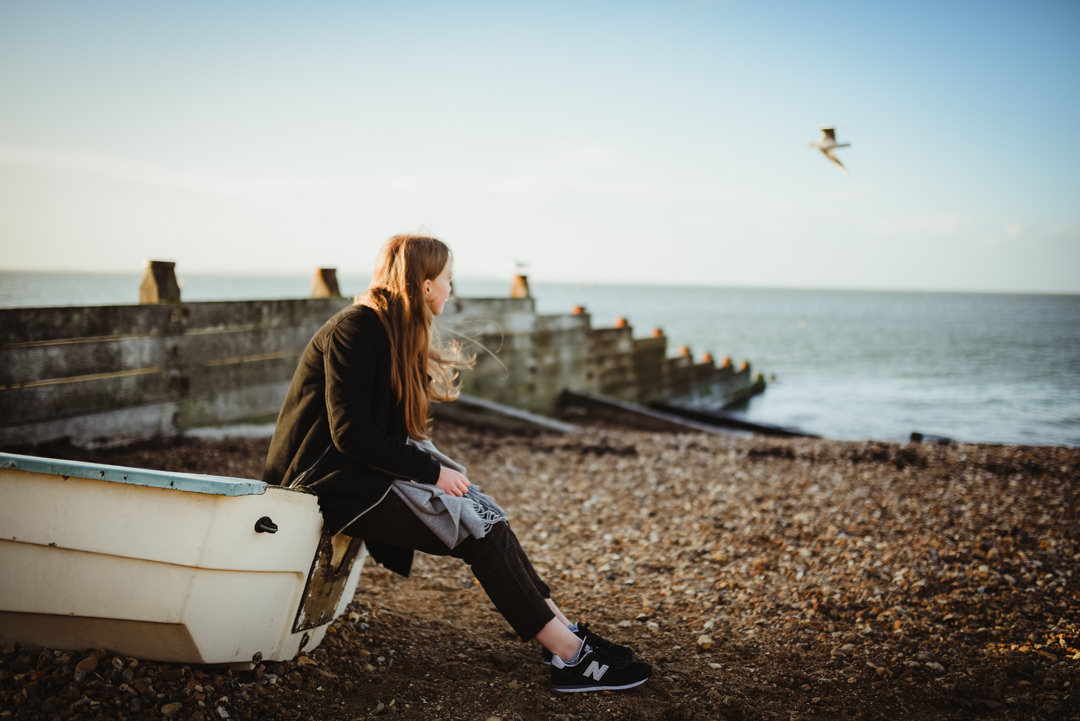 girl sitting on a boat on whitstable beach taken with sigma 35mm lens