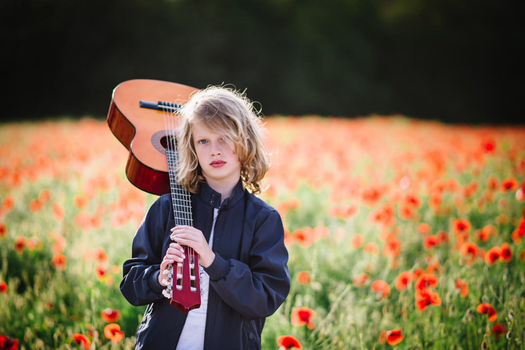 young boy holding his guitar in a sea of poppies