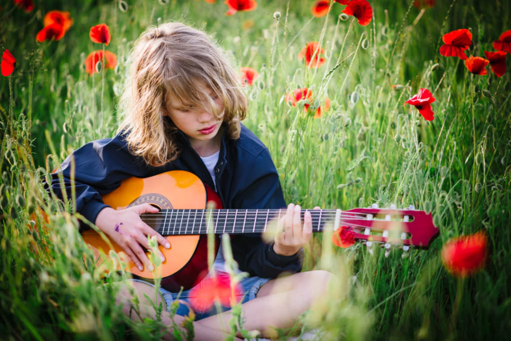 poppy fields surround child playing his guitar in the sunset