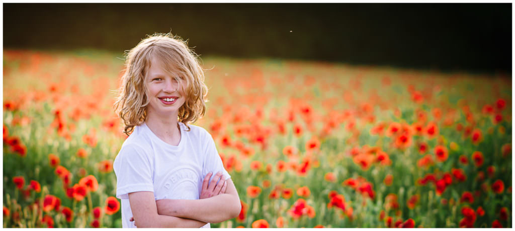a boy smiles on his poppy portrait session in the fields at golden hour