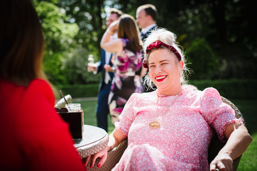 wedding guest dressed all in pink laughs at a joke in the gardens of the bull hotel gerrards cross