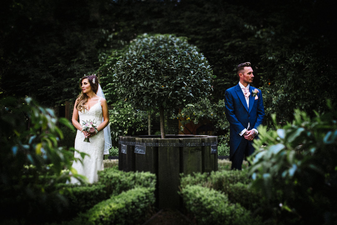 bride and groom pose in the manicured gardens of the bull hotel gerrards cross