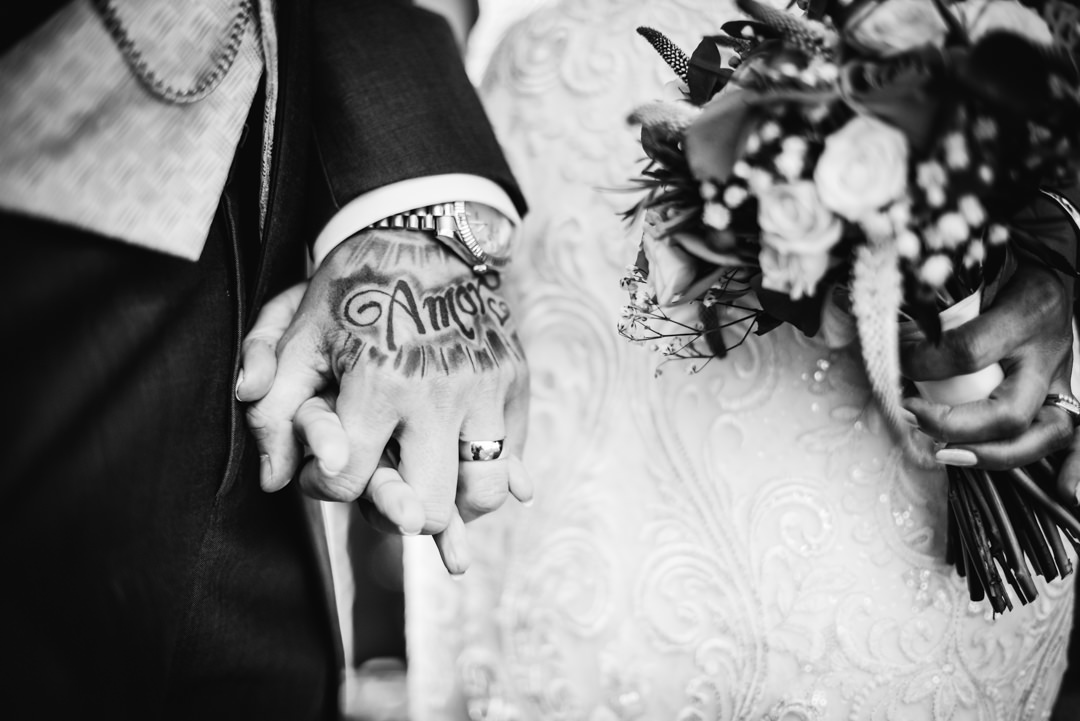 bride and groom hold hands showing his tattoo which spells amore