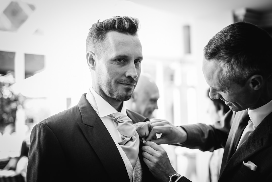 best man attaching button hole to grooms suit lapel at the bull hotel gerrards cross