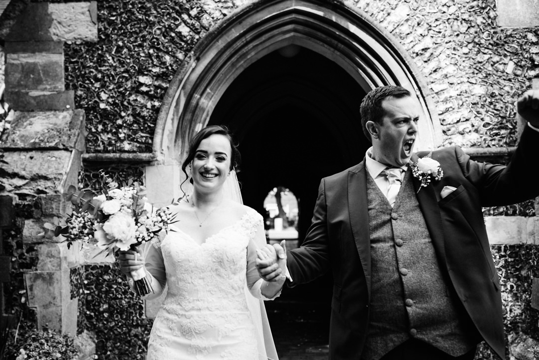 groom fist pumps the air leaving church after wedding