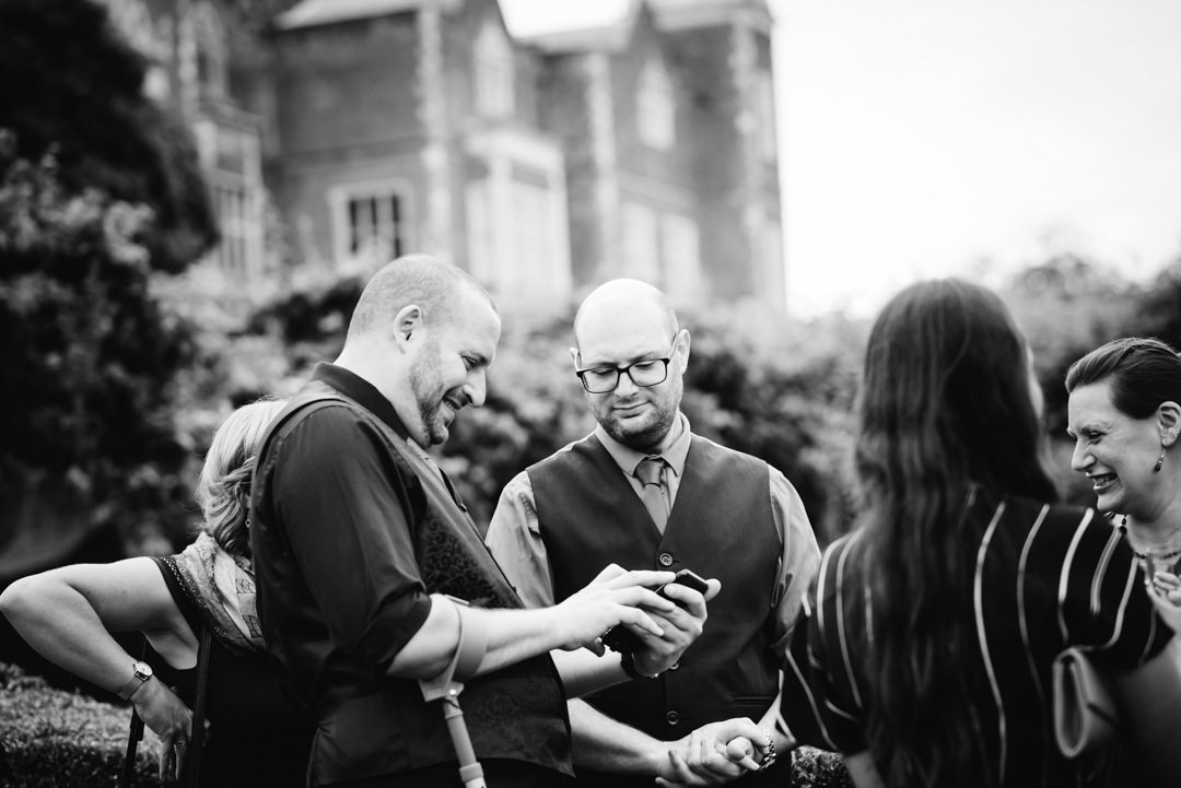 wedding guests look at a phone together with hatfield house coming in the background