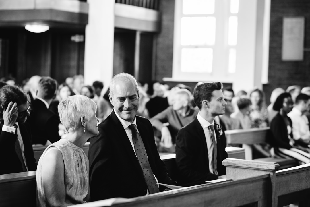 grooms parents smile fondly at each other as the bride and groom take their vows