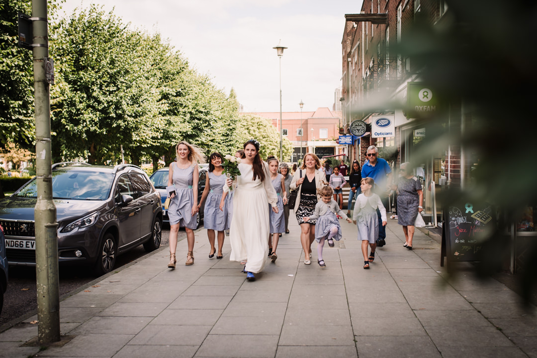 brides walks with her wedding party through welwyn garden city to the church