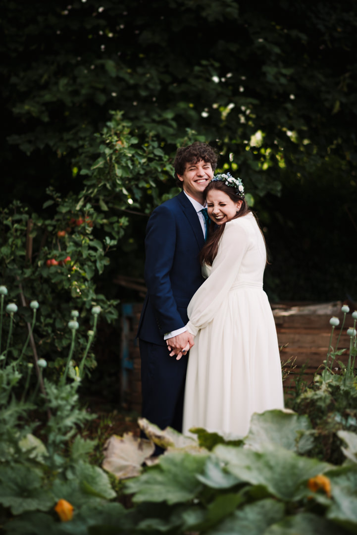 laughing bride and groom stand amongst the veg patch at their welwyn garden city wedding reception