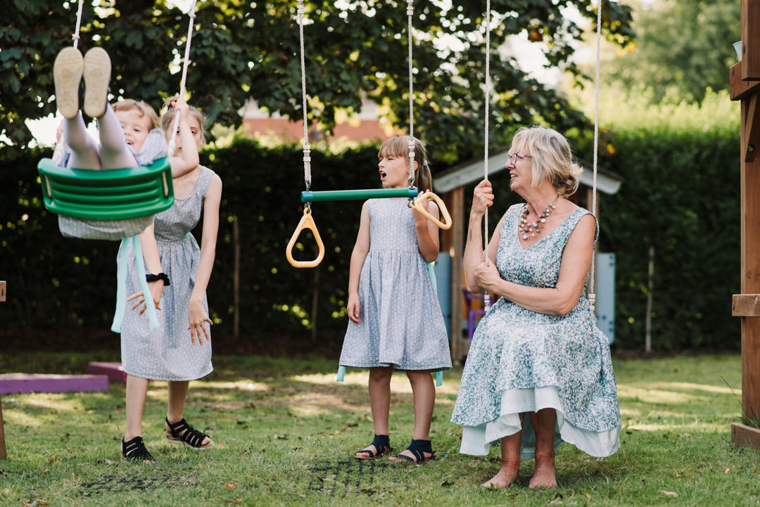 bridesmaid and mother of the bride play on the swings during the garden party reception at the free church welwyn garden city
