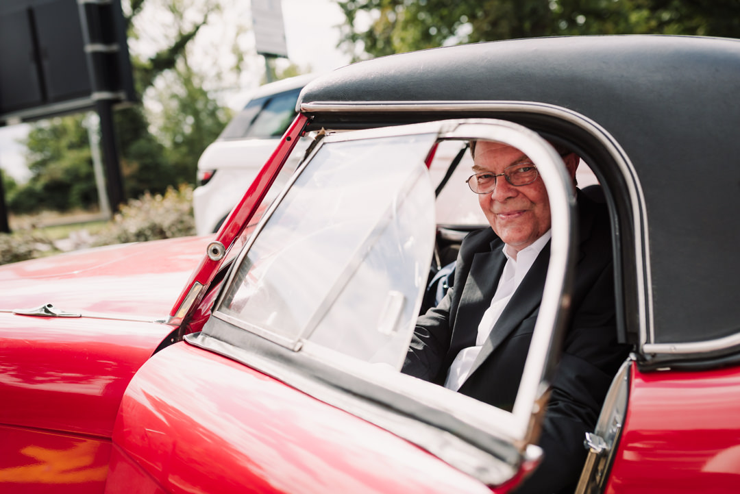 father of the groom arrives in a shiny red classic car