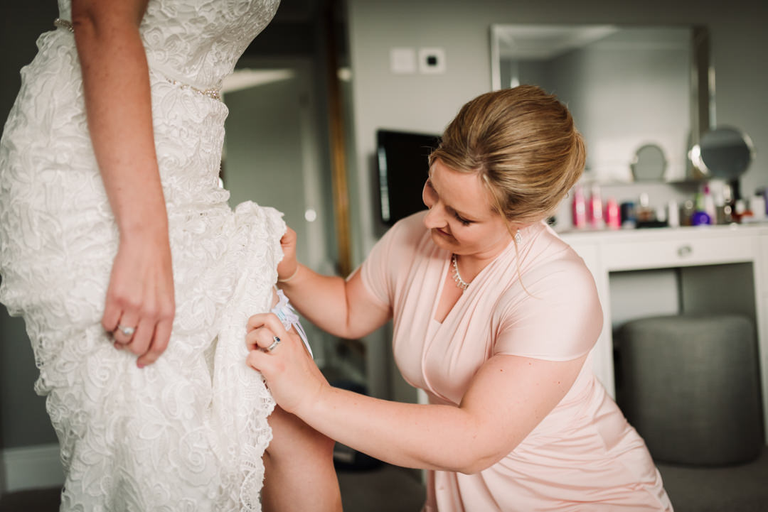 bridesmaid adjusts brides garter before her harpenden wedding 