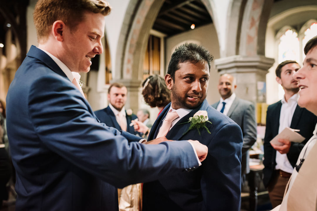 harpenden wedding photographer snaps groom helping best man with his button hole