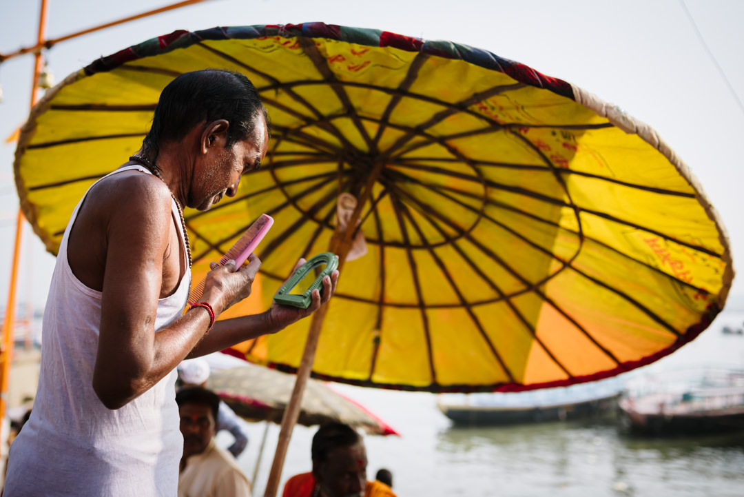 indian man checks his reflection by the ghats in varanasi india