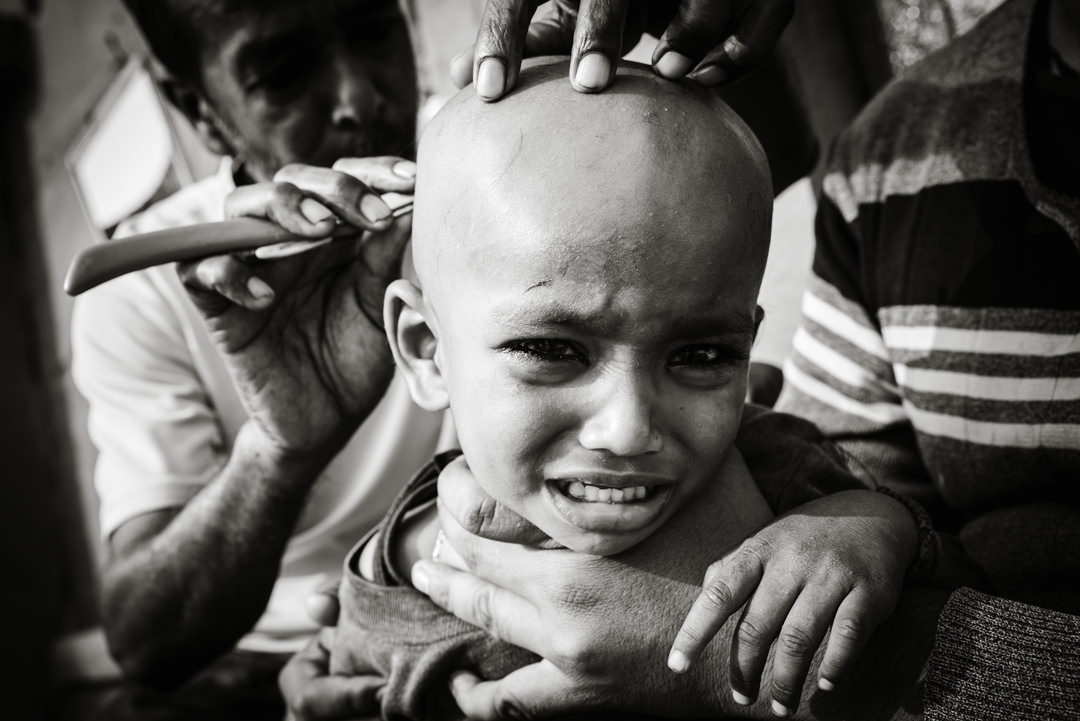 small child cries whilst his head is shaved in varanasi street barbers