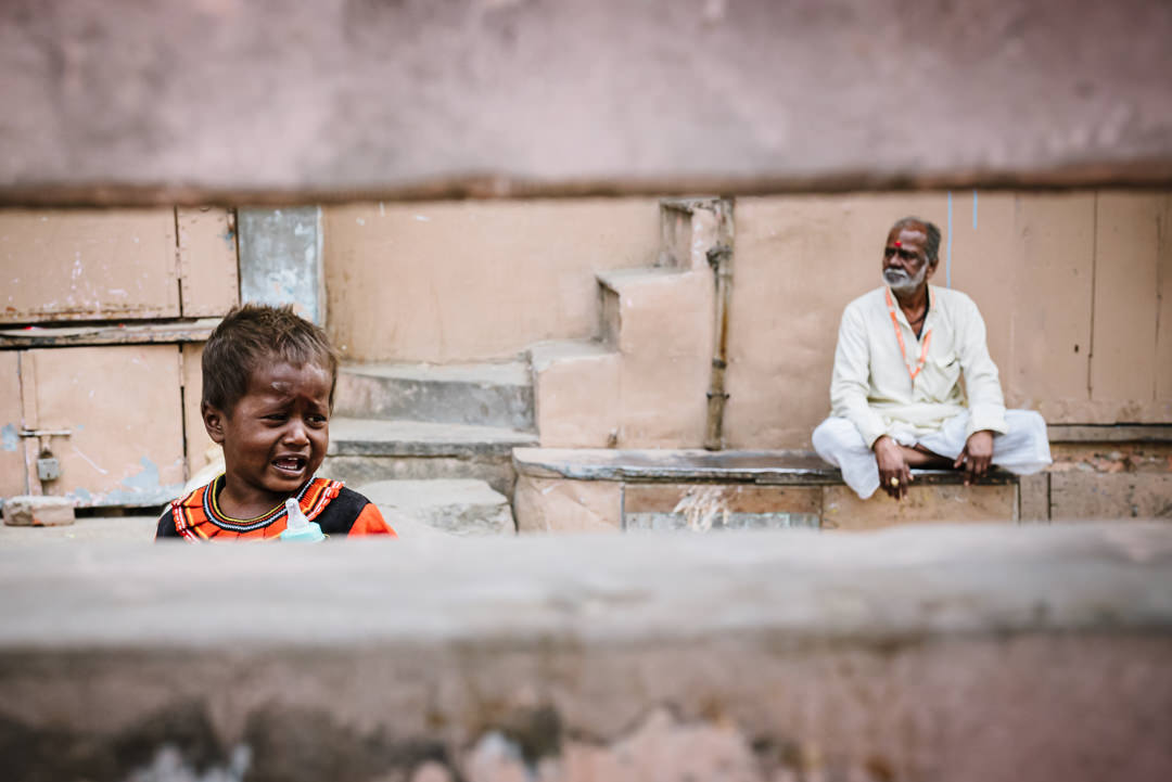 crying street kid is watched by peaceful holy man sitting in a varanasi street