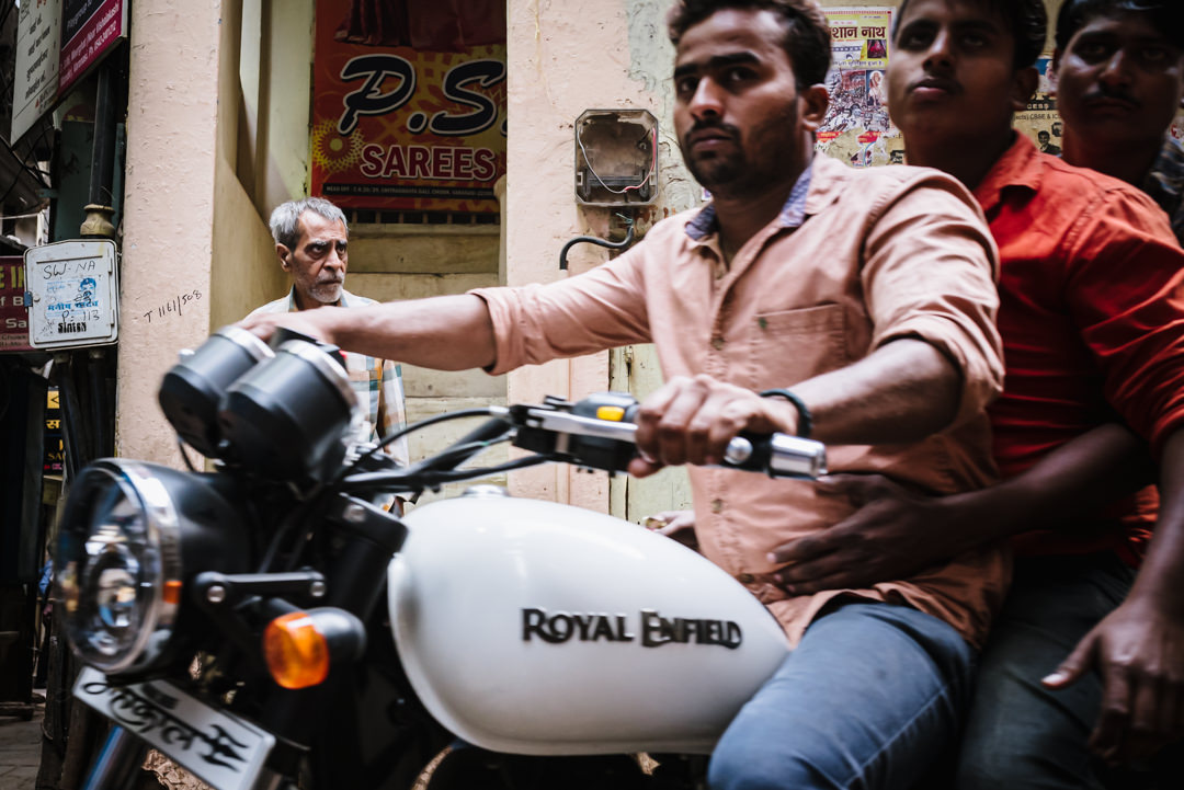 back street in varanasi with royal enfield drivers passing by