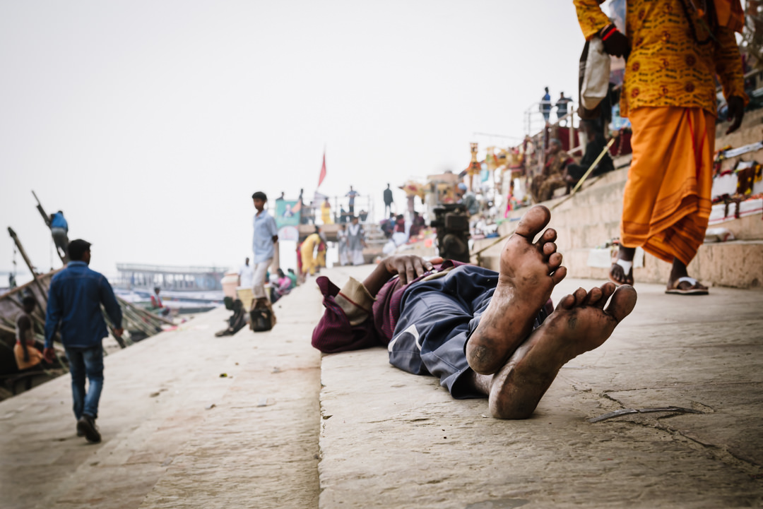 man sleeps with filthy feet up along the street in varanasi india