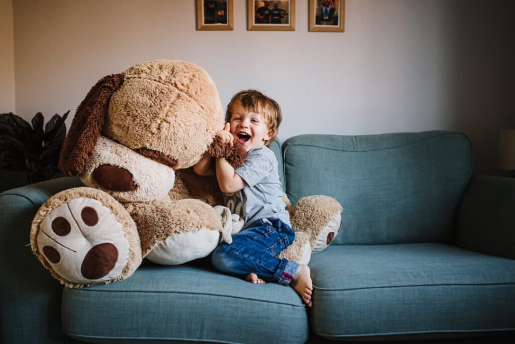 big brother plays with his huge teddy during his newborn photography session in hertfordshire