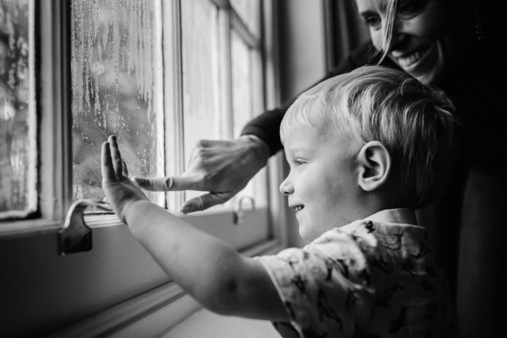 young boy draws on the window pane