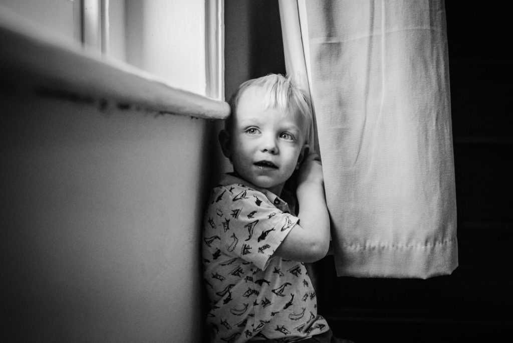 young boy hiding behind the curtain in hertfordshire during a newborn photography session