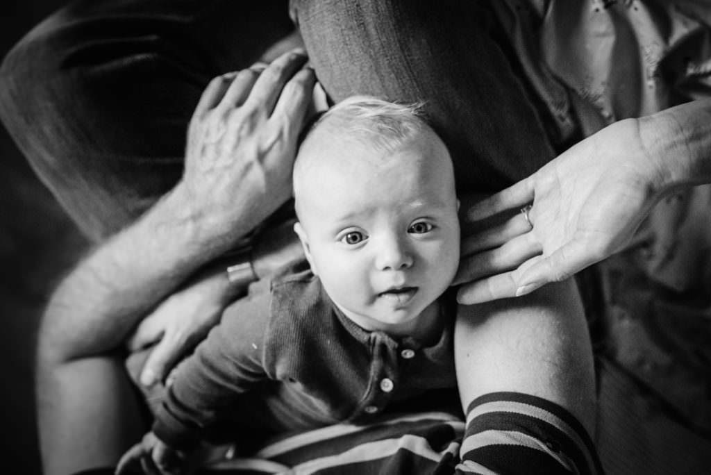 newborn boy looks up to the camera whilst cradled in his parents arms