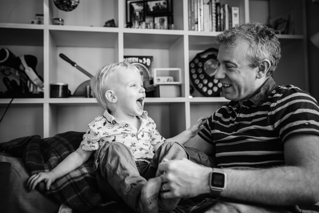 dad and his son laugh on the sofa during their hertfordshire newborn photography session