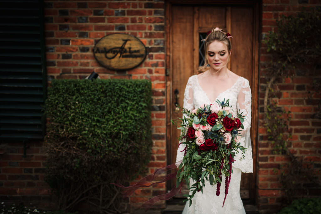 bride stands holding bouquet in front of imposing door at auberge du lac
