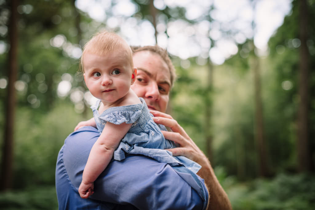 Inquisitive baby looks over her dads shoulder during their family photography session