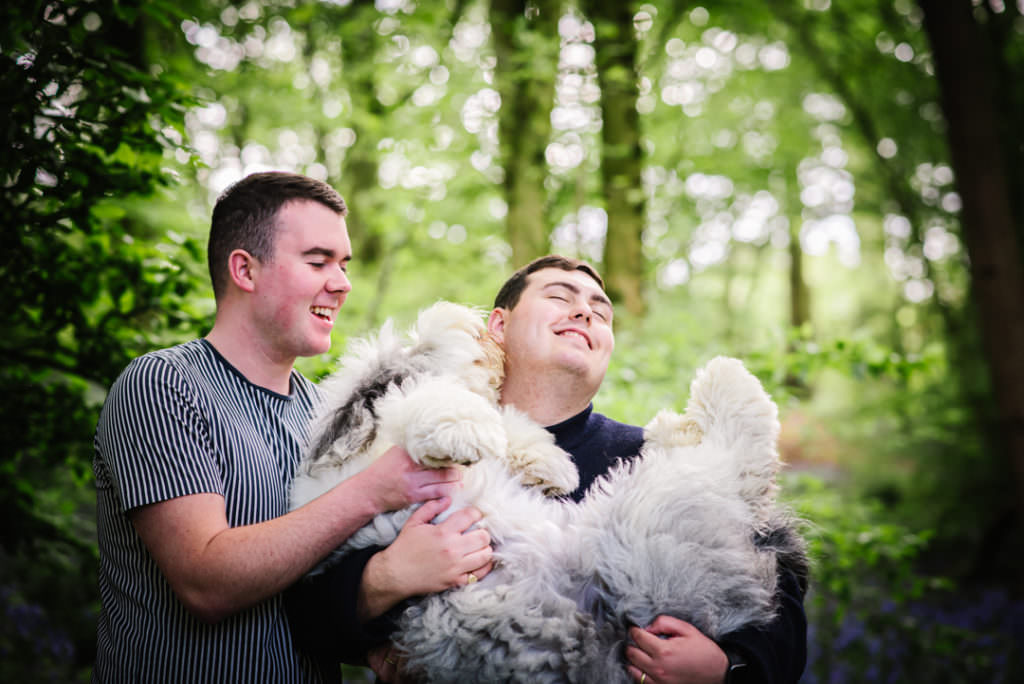 couple cuddle their dog in the bluebell woods during their photo shoot