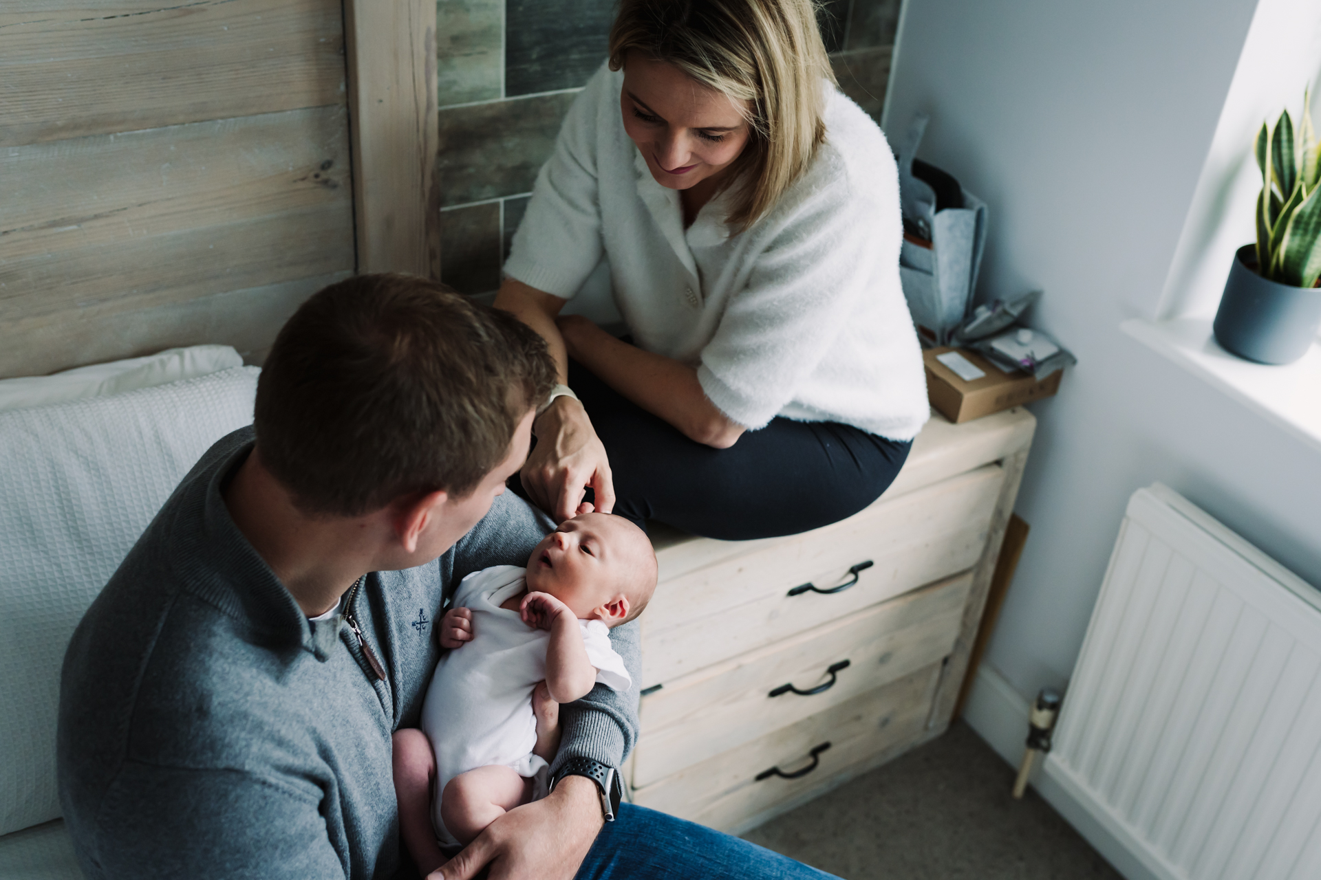 Natural window light illuminates newborn baby and her parents as they enjoy moments together at home