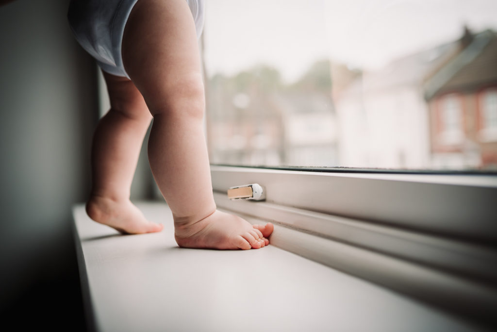 Chubby baby legs standing on a Hertfordshire window sill