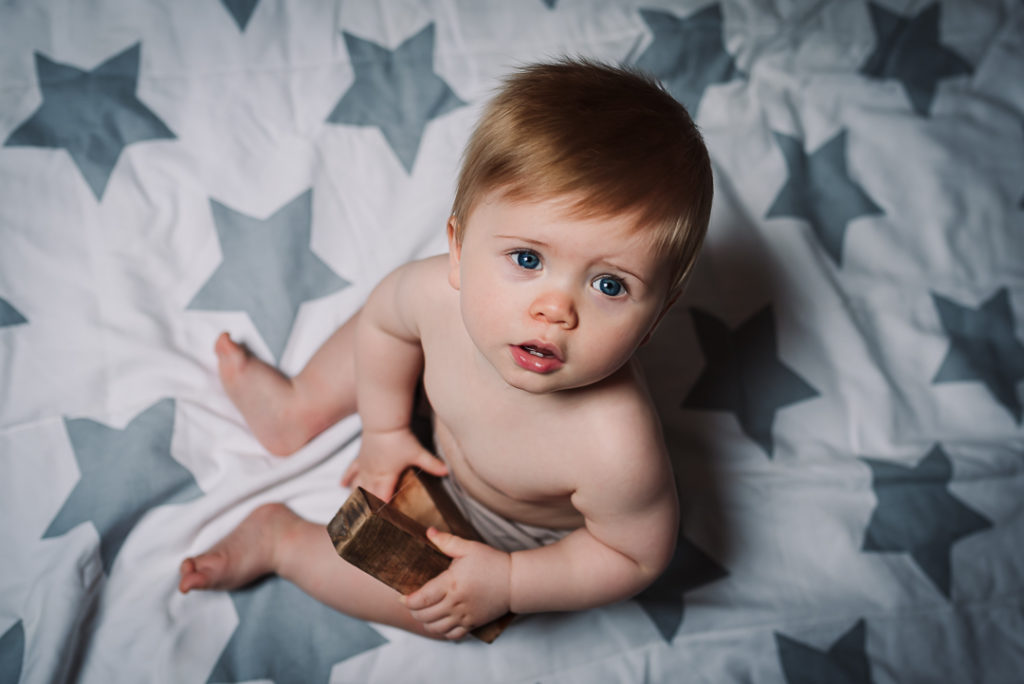 Baby sits on a star blanket whilst looking straight into the camera lens