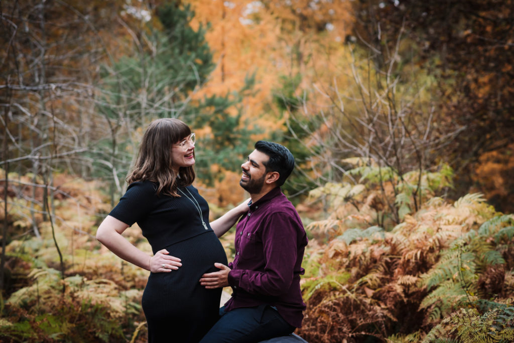 pregnant couple smile at their maternity bump in Hertfordshire woodland location