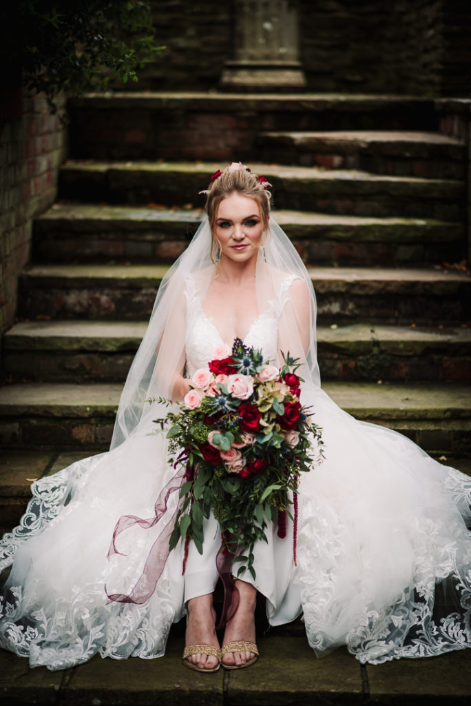 brides sits on steps at wedding venue with her wedding dress spread out around her