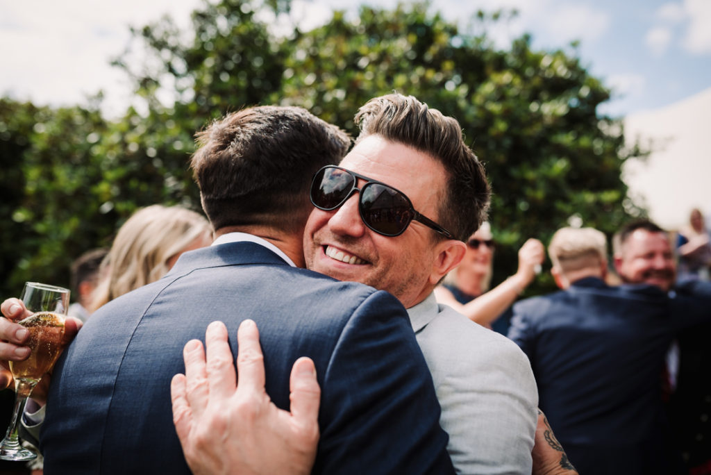 Hugging guests enjoy the sunshine before same sex Hertfordshire wedding