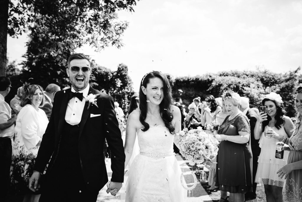 bride and groom walk through confetti in the gardens of gaynes park