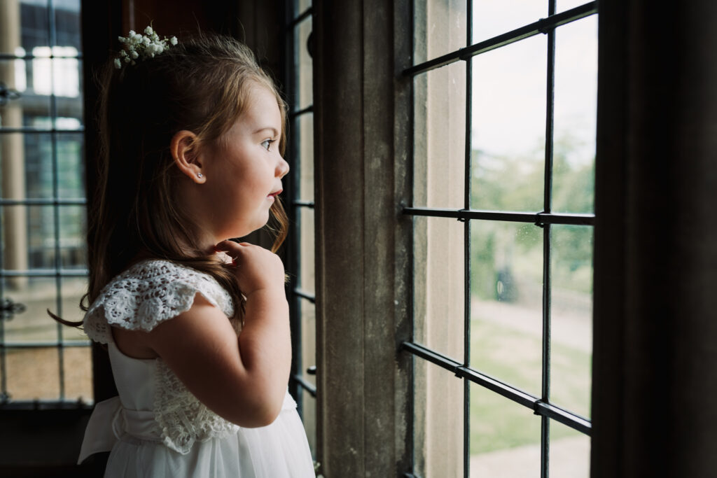 Small bridesmaid looks out of window at Fanhams Hall