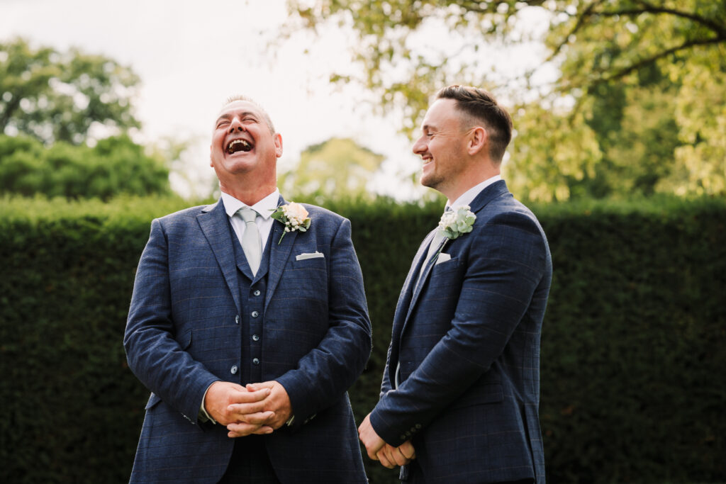 Groom and his best man laugh in the gardens of Fanhams Hall