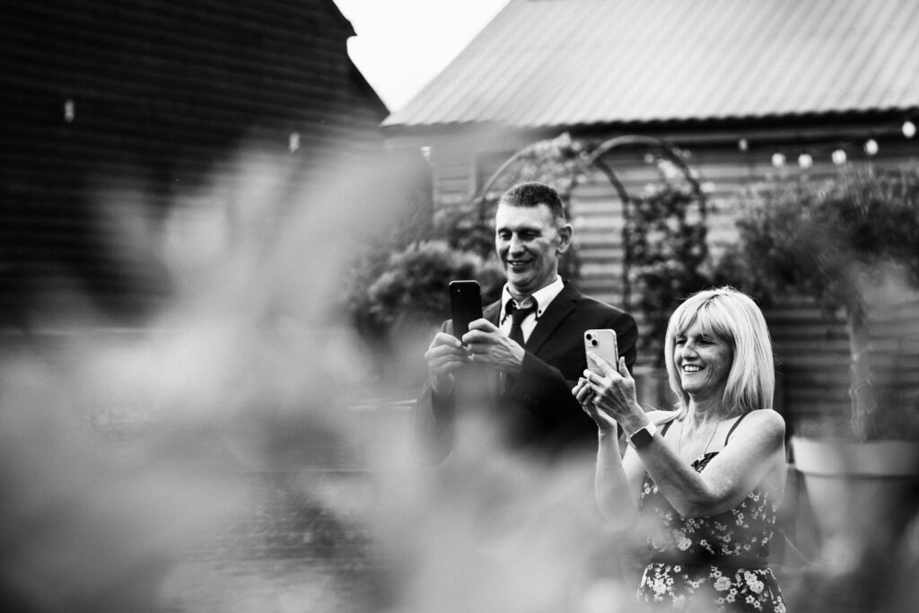 Guests take photographs with their phones at Milling barn wedding reception