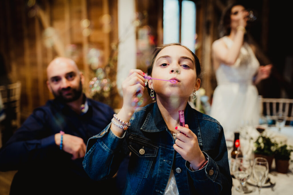 Tewin Bury Farm wedding photographer captures young bridesmaid blowing bubbles