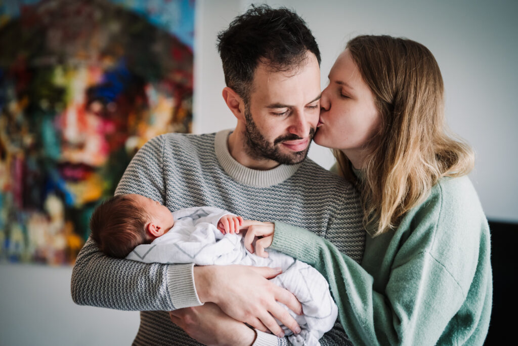 Parents share a kiss holding their newborn baby in Hertfordshire