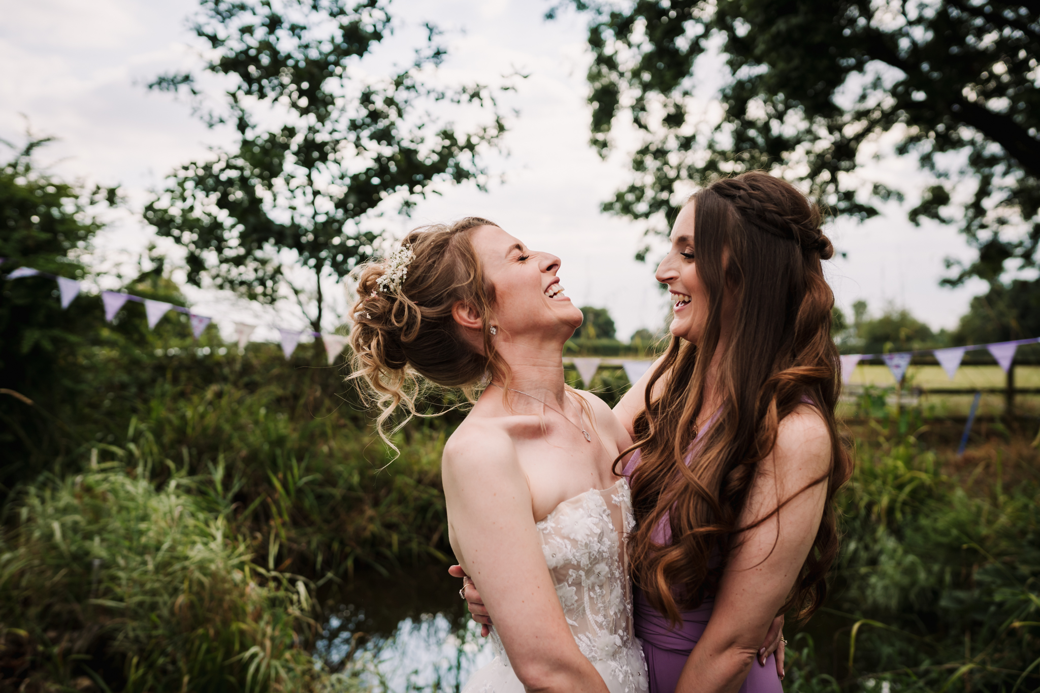 bride and her bridesmaid share a joke in the garden after the wedding ceremony in hertfordshire