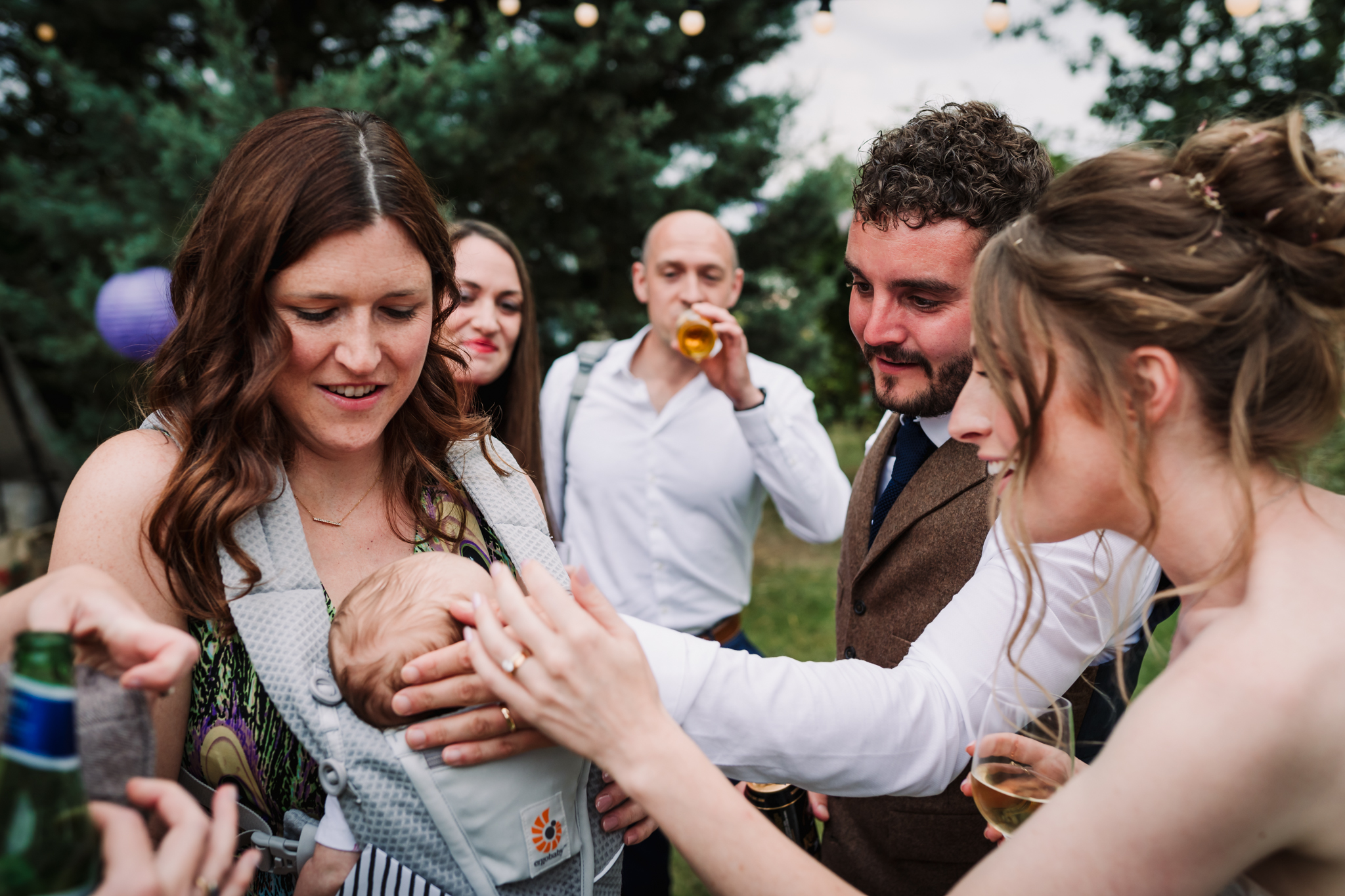 bride and groom admire guests baby during their garden party wedding in hertfordshire