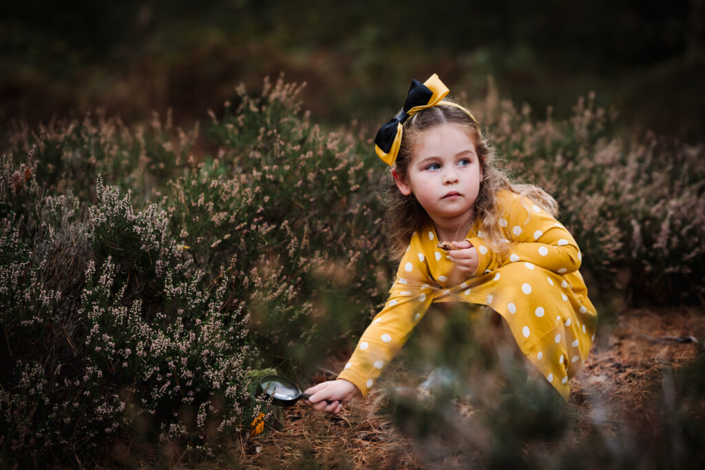 little girl in a yellow dress looks through a magnifying glass on her family photo shoot in hertfordshire