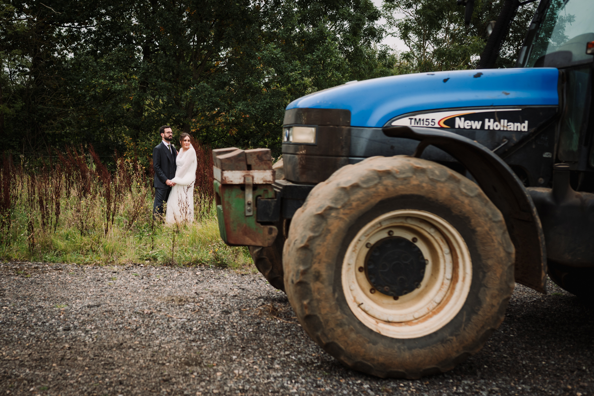 A tractor photo bombs the bride and groom portraits at The Farmhouse at Redcoats in Hitchin